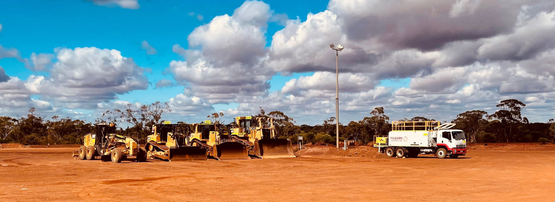 a row of various machines on red dirt with a cloudy sky