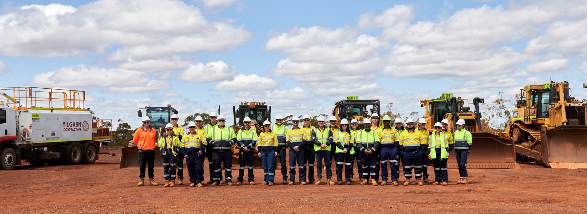 a large group of workers in high vis, in front of mining machinery